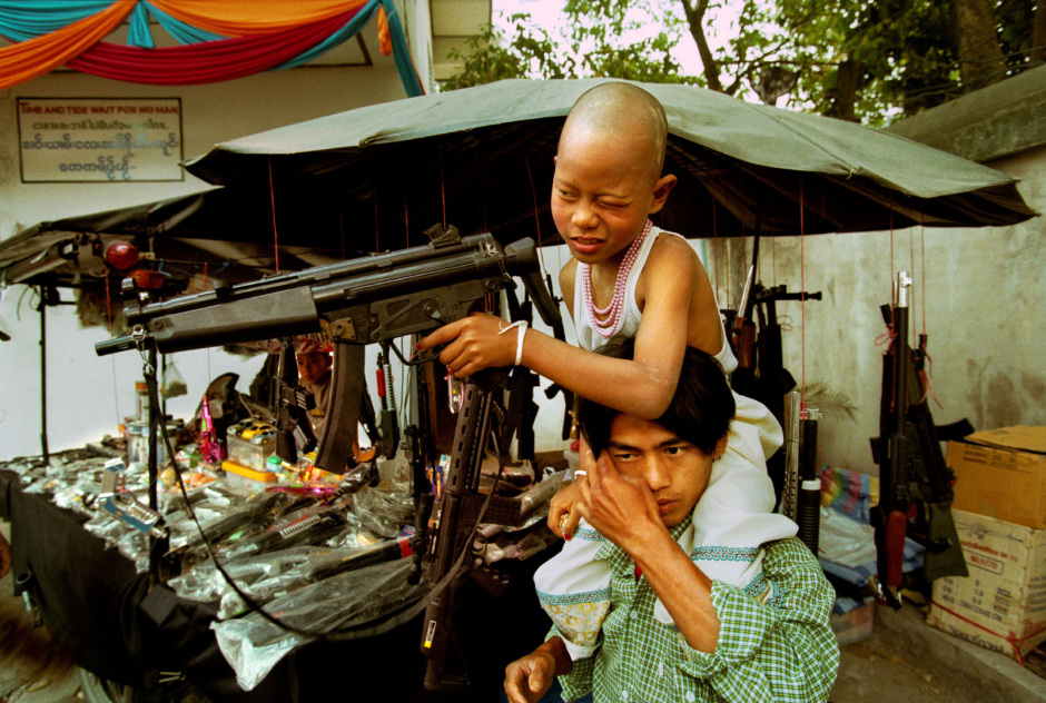 Thailand, Chiang Mai, 2002Shan Buddist Ceremony for young novice monks held at WatPa Pao in Chiang Mai,north-western Thailand.The ceremony takes place over three days where children are dressed up with lavish clothing and bright makeup and carried on the shoulders of family members.Photo shows a young novice monk on the shoulders of a family member after just buying a toy gun before the start of the ceremony.Thailande, Chiang Mai, 2002Une cÈrÈmonie bouddhiste Shan pour les nouveaux moines se passe au temple WatPa Pao ‡ Chiang Mai, au Nord-Ouest de la Thailande. La cÈrÈmonie dure 3 jours et les enfants sont habillÈs de vÍtements lourds, sont maquillÈs avec des couleurs voyantes et sont portÈs sur les Èpaules des membres de leur famille. Un jeune novice sur les Èpaules d'un membre de sa famille aprËs l'achat d'un fusil en plastique avant le dÈbut de la cÈrÈmonie.Steven Siewert / Agence VU