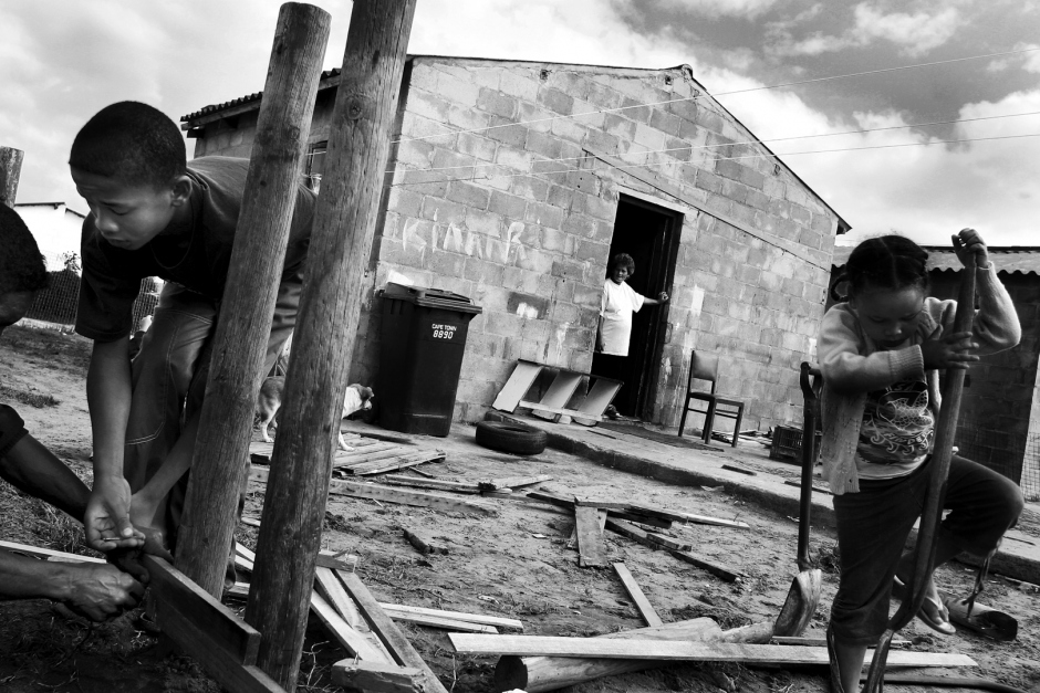 South Africa, Atlantis, april 2004Douglas Jacobs and his son Blaine make repairs to the house fence, while his daughter Chantal plays nearby. His wife Elizabeth is watching from the house.  Afrique du Sud, Atlantis, Avril 2004Douglas Jacobs et son fils Blaine font des repÈrages pour la clÙture de lamaison, alors que sa fille Chantal joue aux alentours.  Sa femme Elizabeth regarde depuis la maison.© Guy Tillim / Agence VU