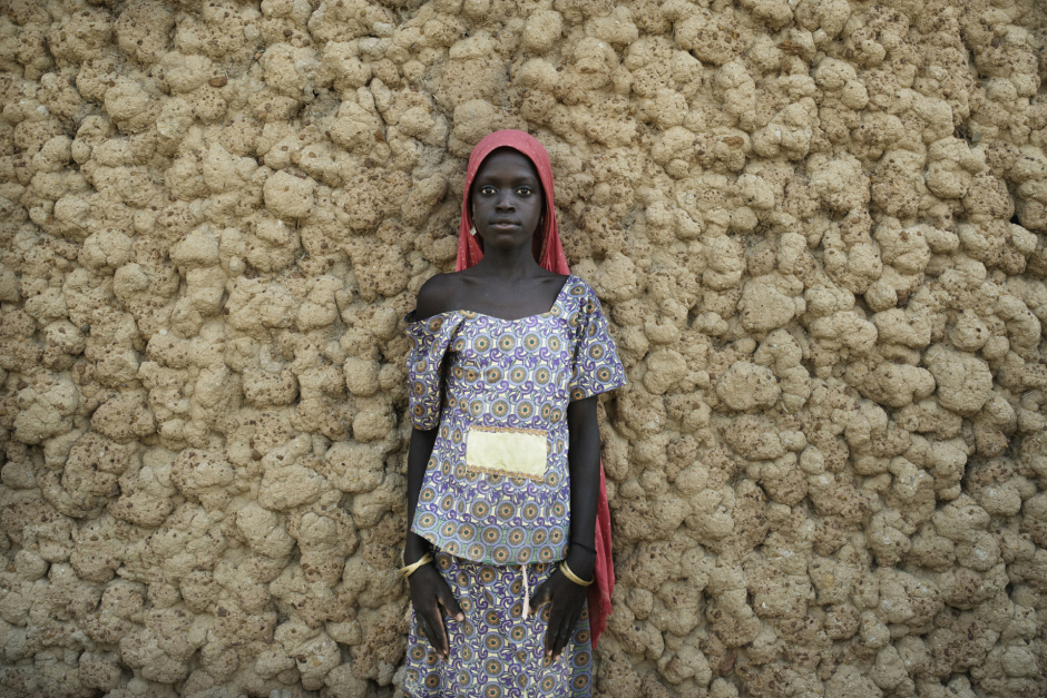 Niger, Zinder, Ragana, June 24th 2016In the Ragana village, where many inhabitants left, at their owns risks, to beg in Algeria (14 people of the village died in the journey to Algeria in June 2016), Wassila Matou, 13 years old, poses in front of their house.She went in Algeria with her mother, and came back. With the money gathered, they bought a calf.Niger, Zinder, Ragana, 24 juin 2016Dans le village de Ragana d'où partent de nombreuses habitantes partent  vers l'Algérie pour aller mendier (14 personnes de ce village sont mortes sur le trajet en juin 2016), Wassila Matou, 13 ans, pose devant sa maison.Avec sa mère, elles sont parties en Algérie et en sont revenues. Avec l'argent récolté, elles ont pu acheter un veau. Michaël Zumstein / Agence VU