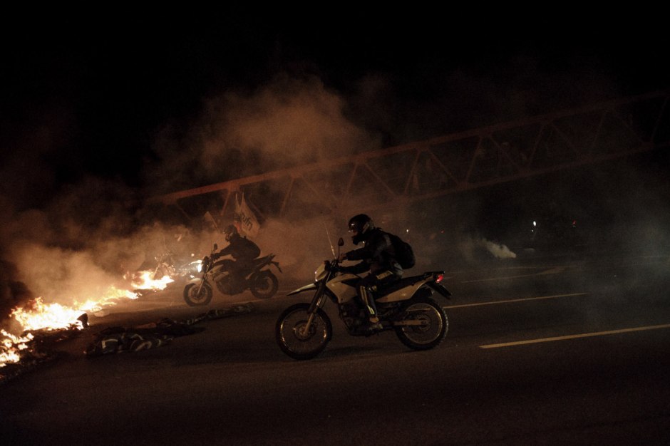 Brazil, Rio de Janeiro, June 30, 2017In the bowels of Brazilian inequality, in the difficulty of remembering our history, our origins, anomia generates the feeling of that « which must not be named ». It occurs when individuals feel pressured to violate norms.Motorcyclists cross a burning tire barrier during clashes between police and demonstrators during a general strike in the outskirts. Brésil, Rio de Janeiro, 30 juin 2017Dans les entrailles de l'inégalité brésilienne, dans la difficulté de se souvenir de notre histoire, de nos origines, l'anomie, engendre le sentiment de ce "qui ne doit pas être nommé". Elle se produit lorsque les individus se sentent incités à violer les normes.Des motards franchissent une barrière de pneus en feu lors d'affrontements entre la police et les manifestants lors d'une grève générale dans la périphérie de la ville. Francisco Proner / Agence VU
